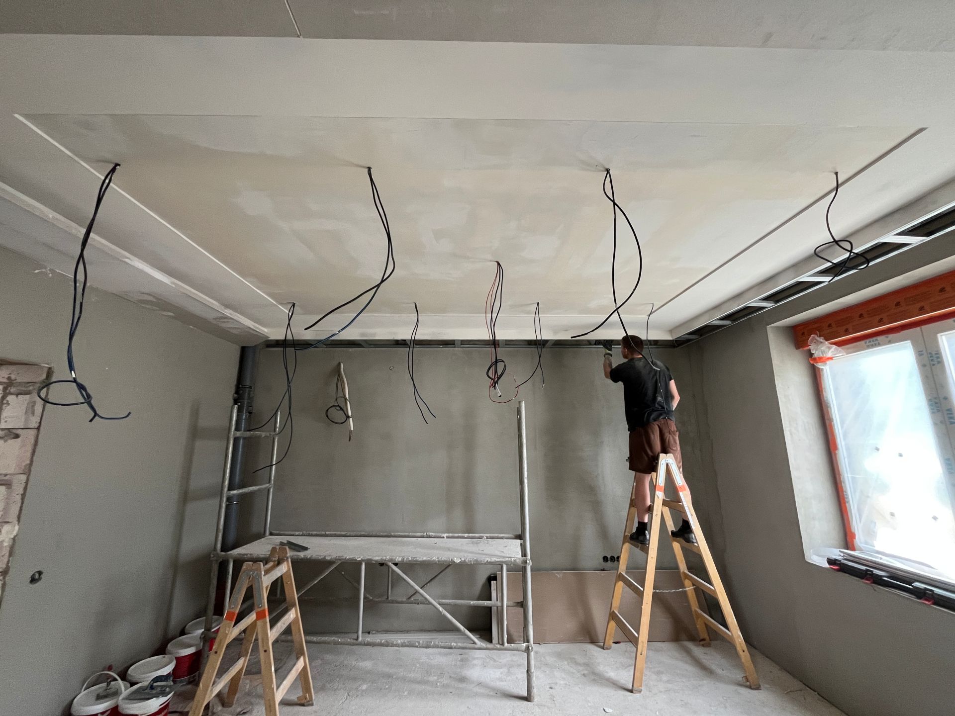 Hotový sádrokartonový strop, kabely na osvětlení, řemeslník na štaflích brousí stěnu